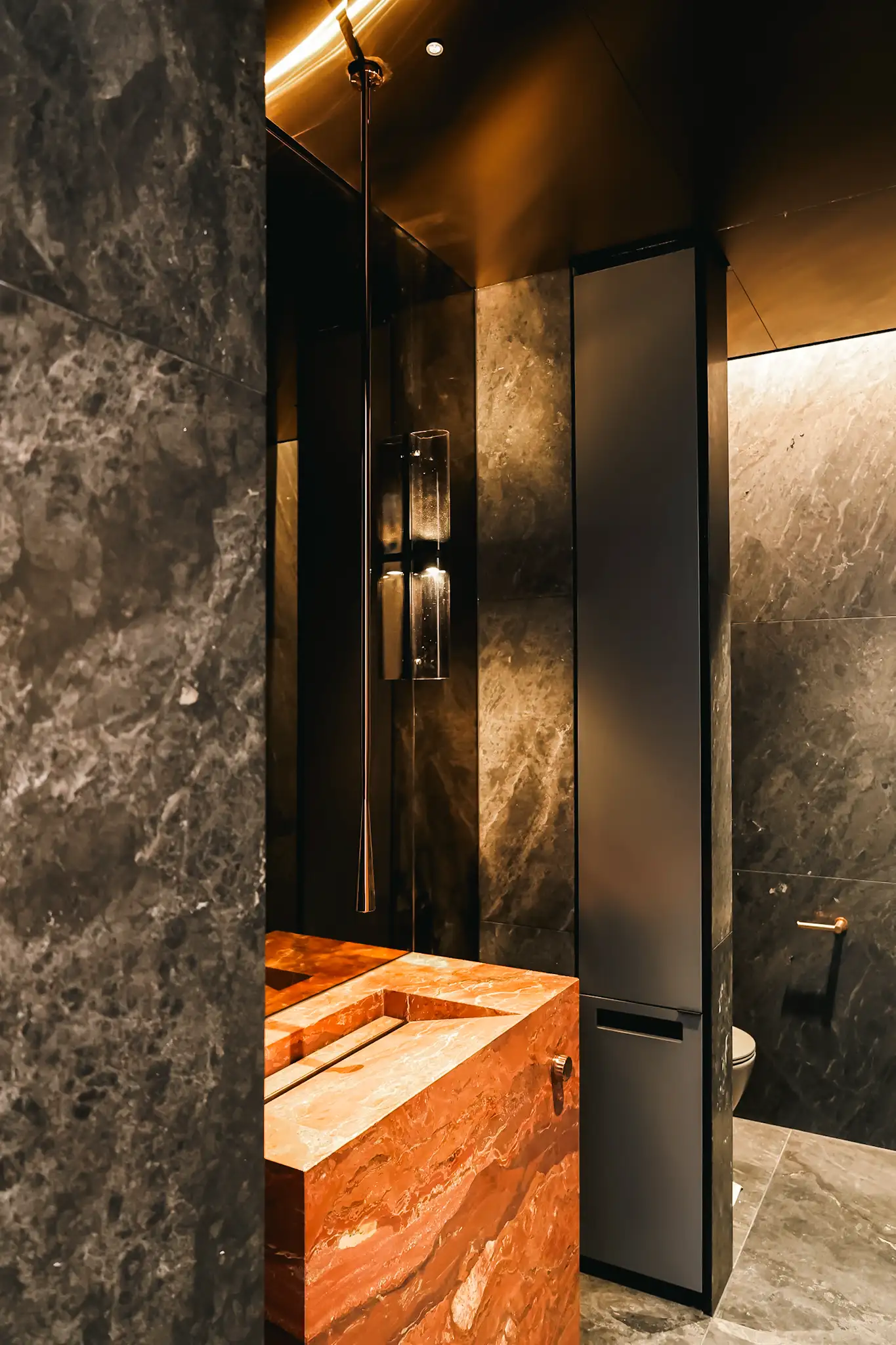 Modern bathroom with dark marble walls, a red marble sink, and a tall black cabinet.