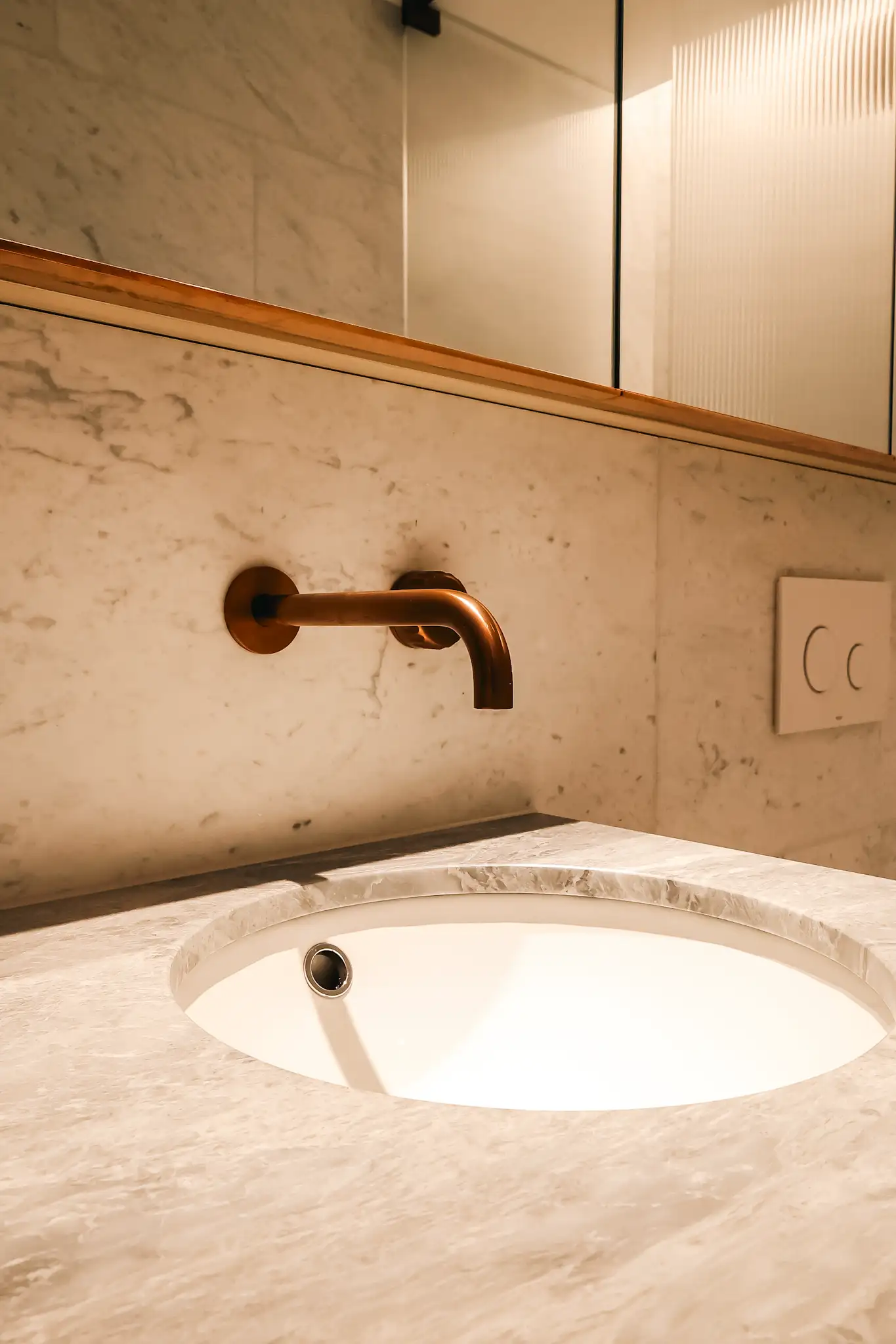 Modern bathroom sink with white marble countertop and copper wall-mounted faucet.