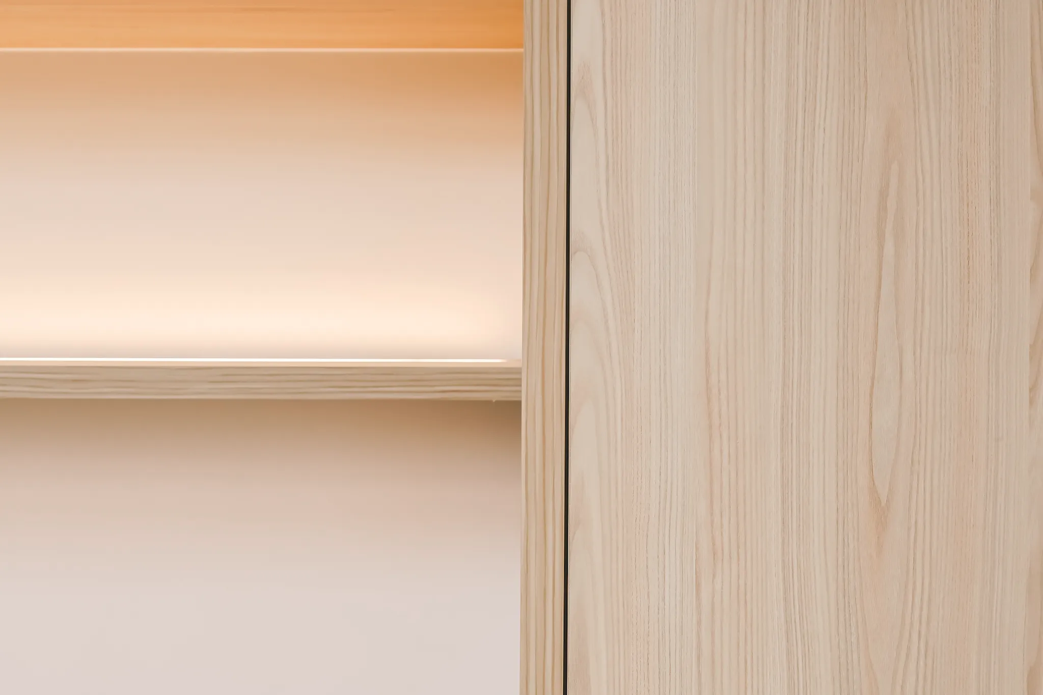 Minimalist wooden shelf with soft warm lighting against a light wood panel background.