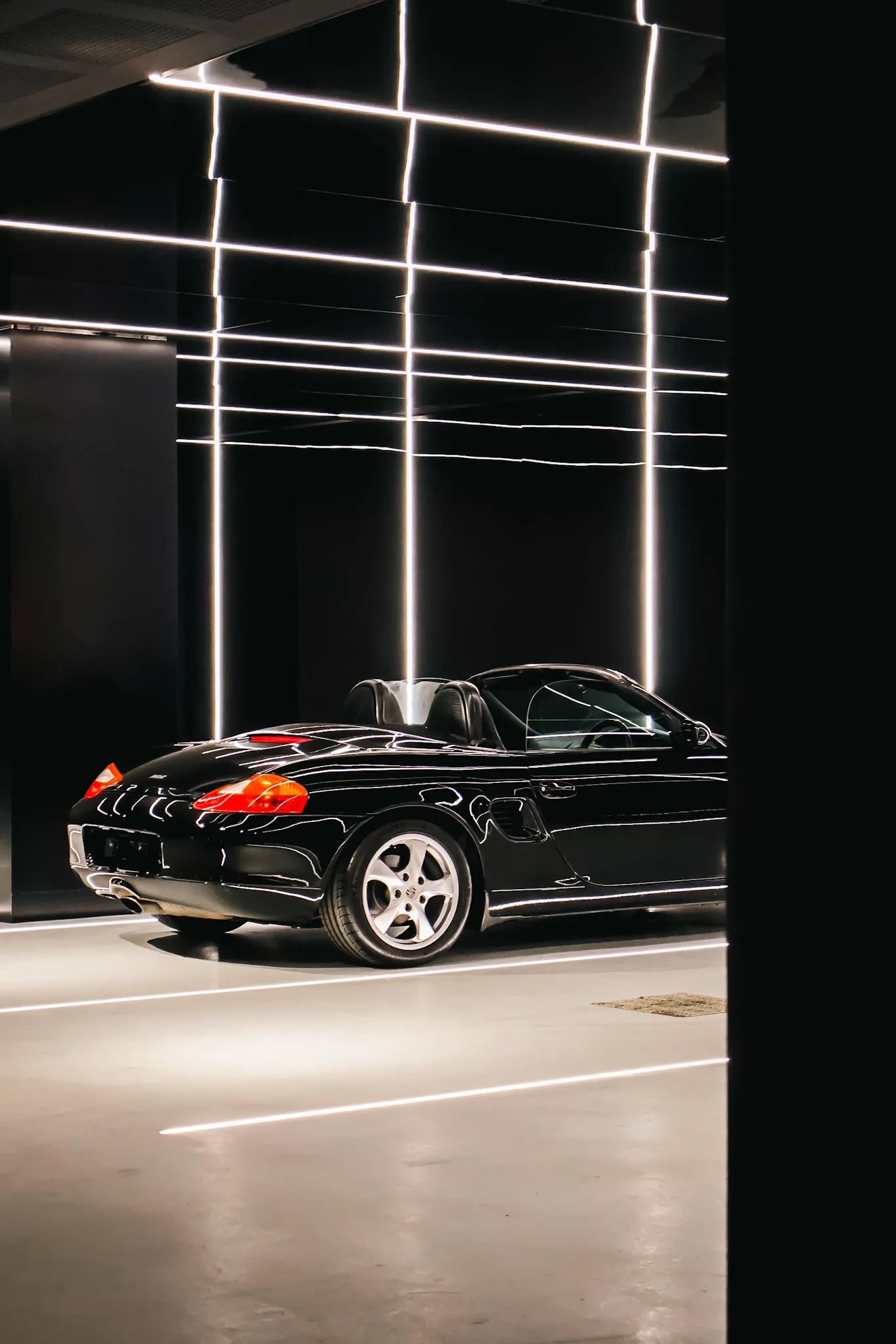 Black convertible sports car parked indoors under vertical and horizontal white LED light strips.