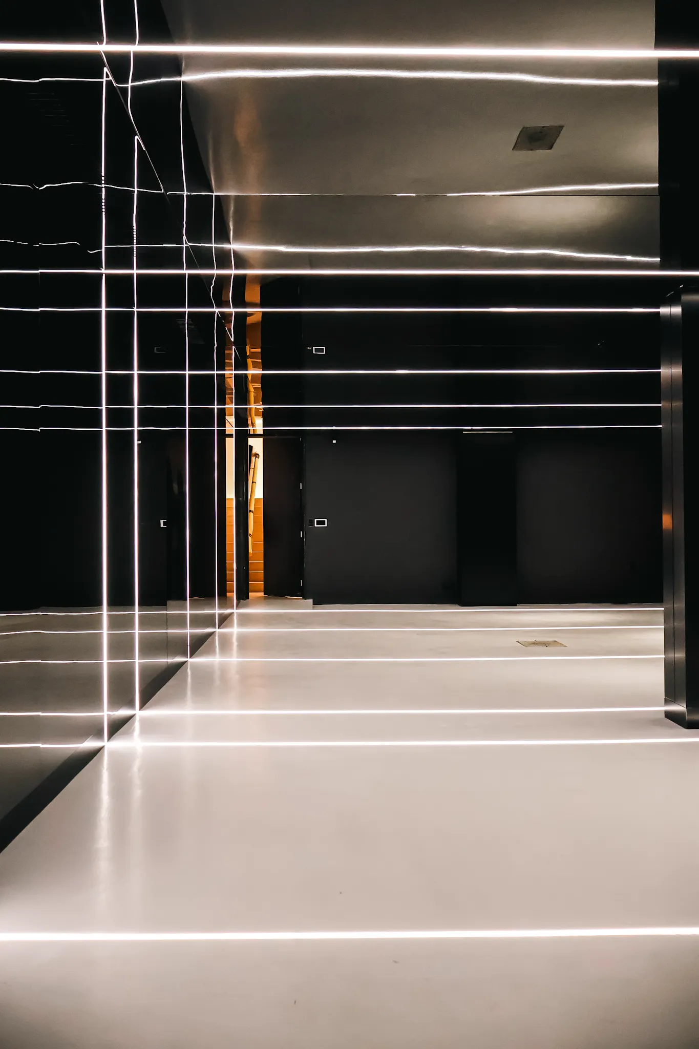 Modern interior hallway with black walls and floor illuminated by horizontal white linear LED lights.