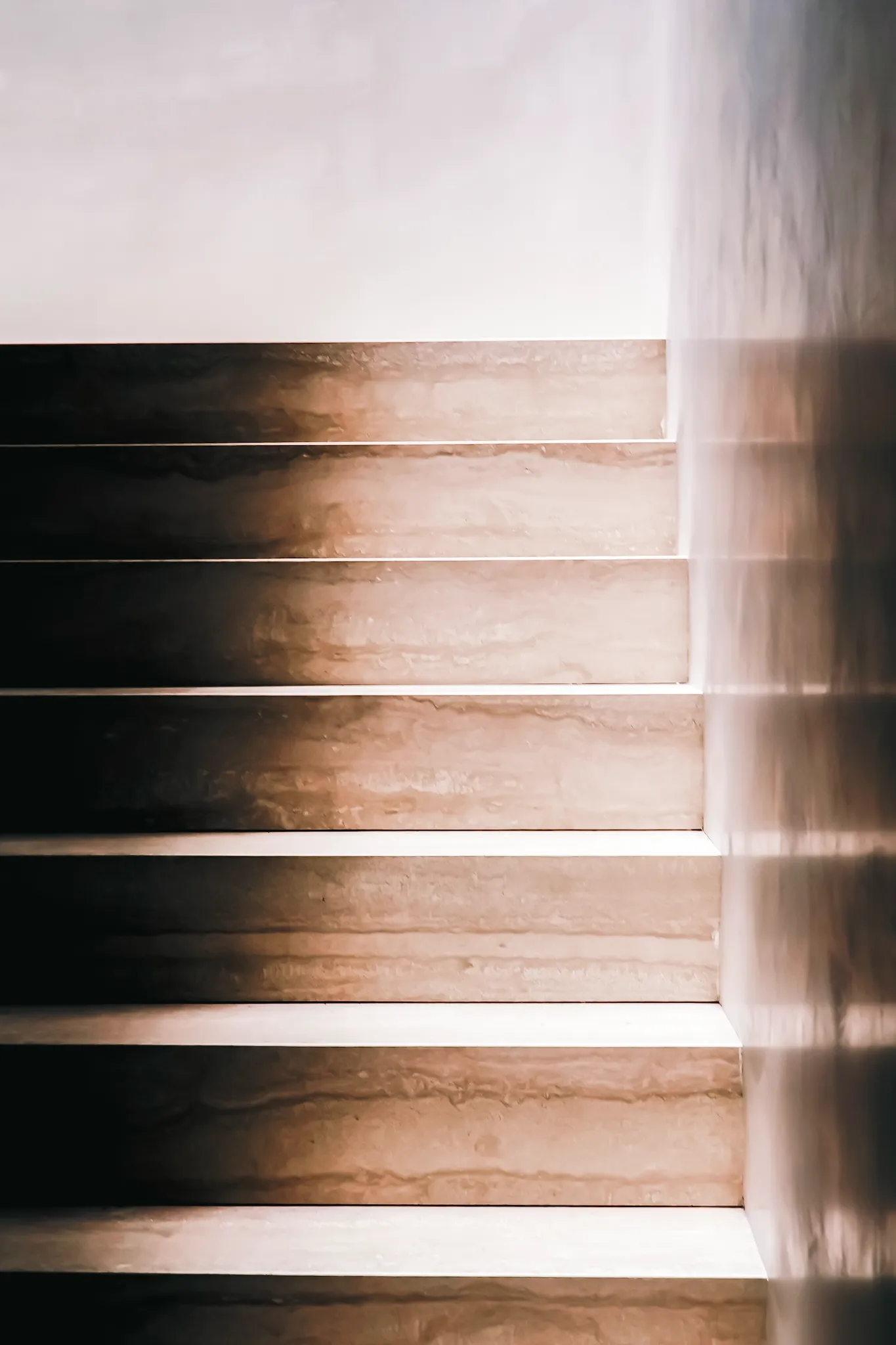 Minimalist stone stairs with soft natural light and shadow along a smooth wall.