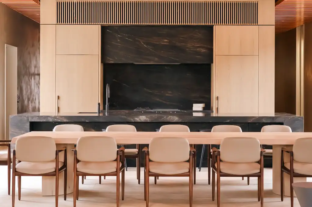 Modern dining area with wooden table and beige chairs in front of a black marble kitchen island and light wood cabinetry.